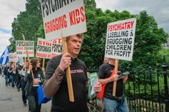 Protesters carry signs opposing psychiatric drugging of children.