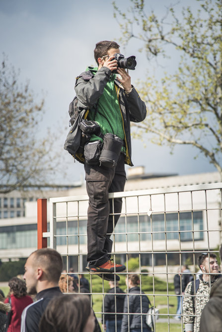A photo journalist standing on a fence to get a shot