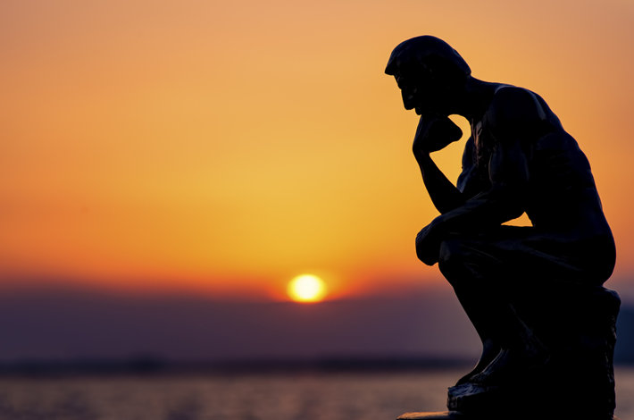Statue of a thinking man against a sunset