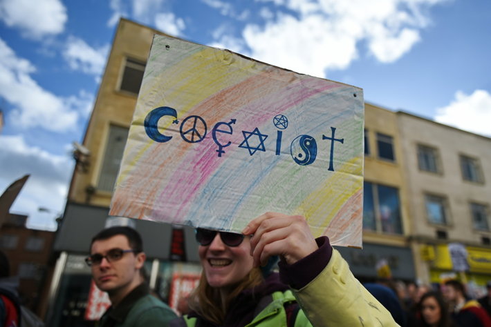 A woman holds a sign that says coexist with the letters made into different religious symbols