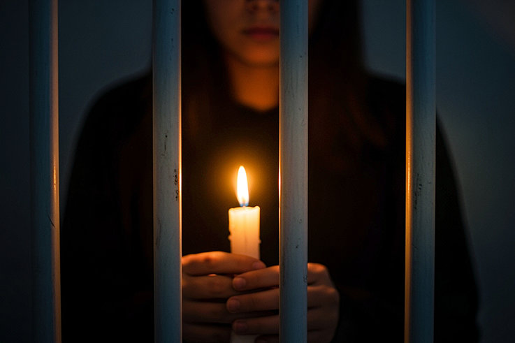 Girl behind bars holding a candle
