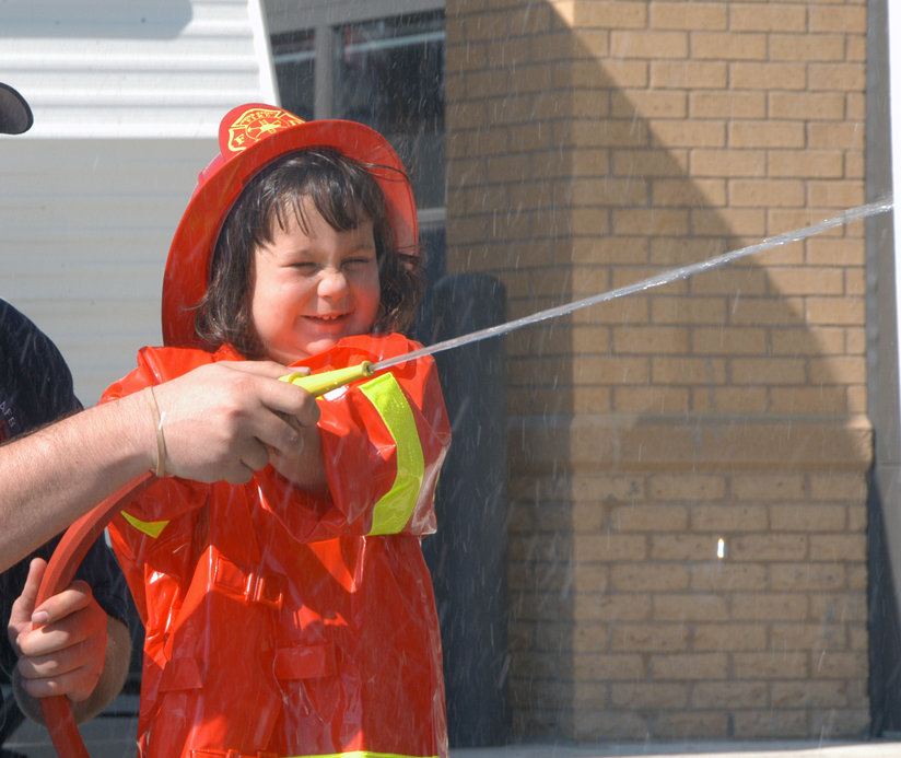 A little girl in firefighter’s uniform with a hose