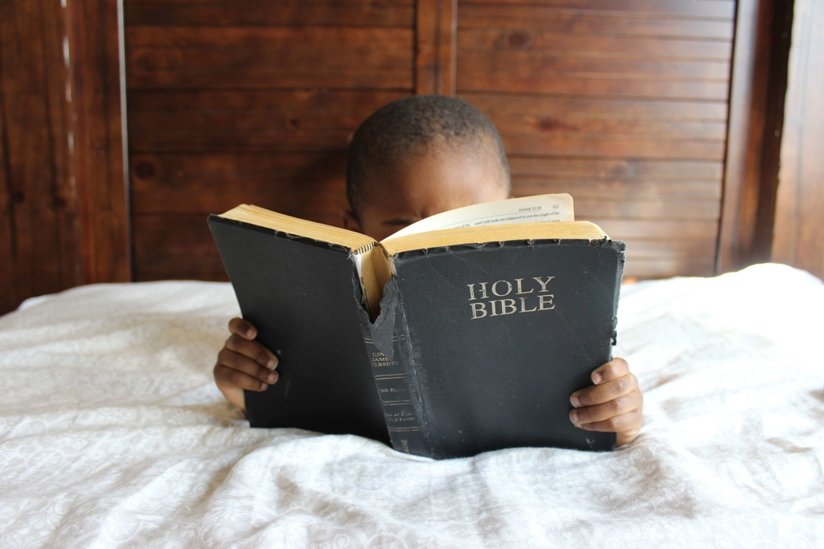 Little boy reading the Bible in bed
